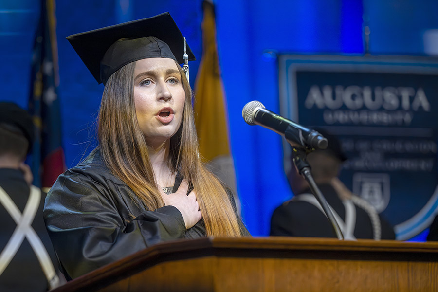 woman standing at a podium with her hand over her heart. 