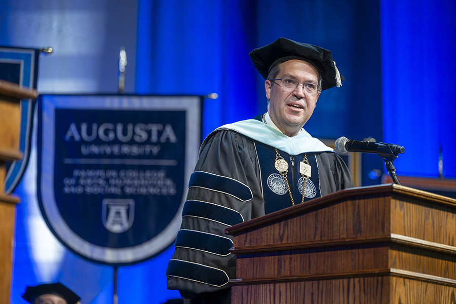 man in a graduation cap and gown standing at a podium. 