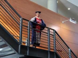 Woman stands in full DNP regalia on staircase, smiling.