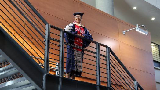 Woman stands in full DNP regalia on staircase, smiling.