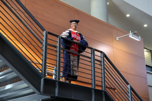 Woman stands in full DNP regalia on staircase, smiling.
