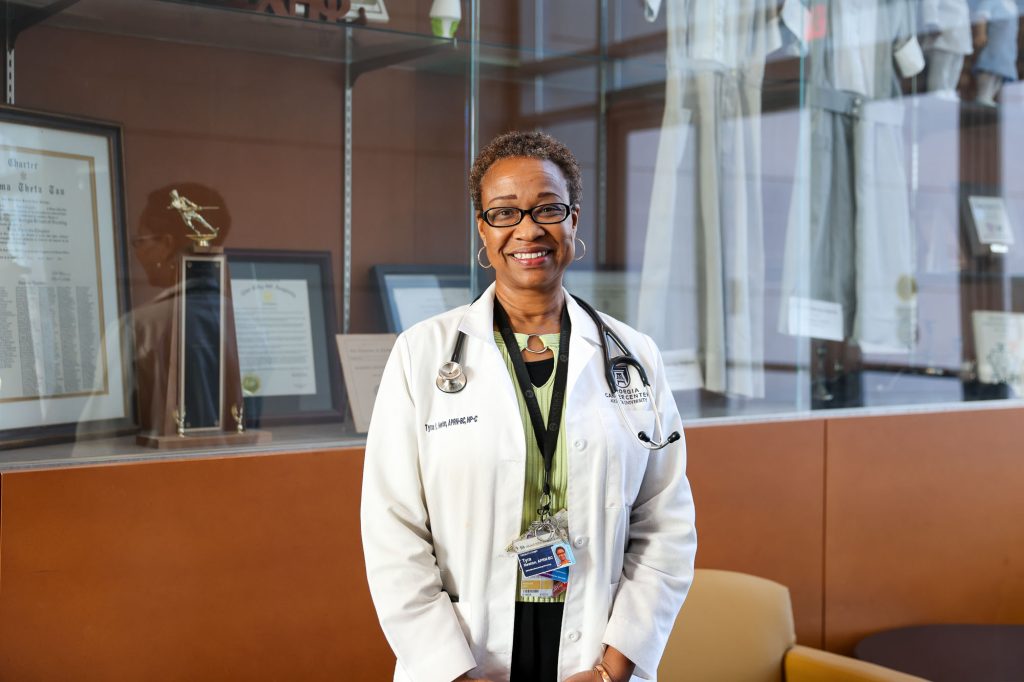 A female doctor wearing her lab coat stands in the entryway of a modern building.