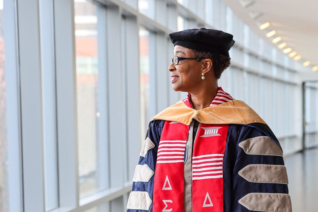 A woman wearing full graduation regalia for a Doctor of Nursing Practice candidate looks out of a window