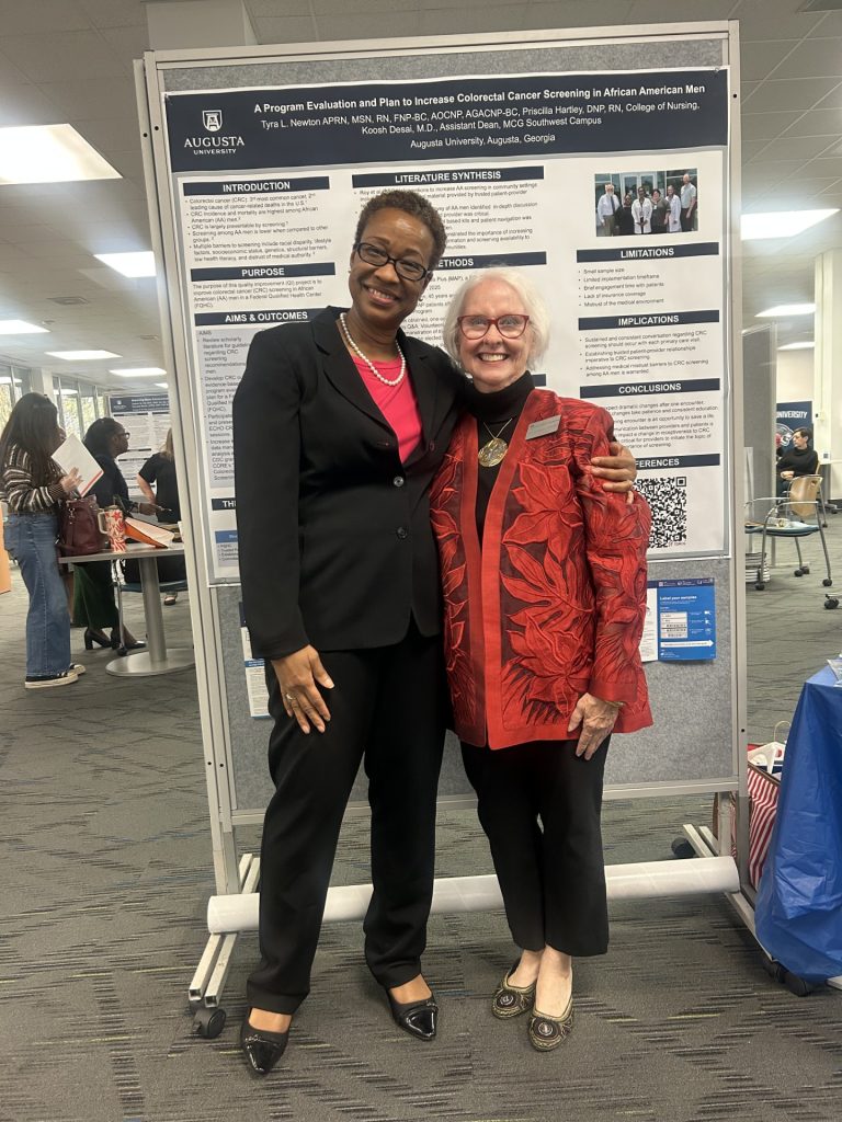 Two women stand smiling in front of research poster.

