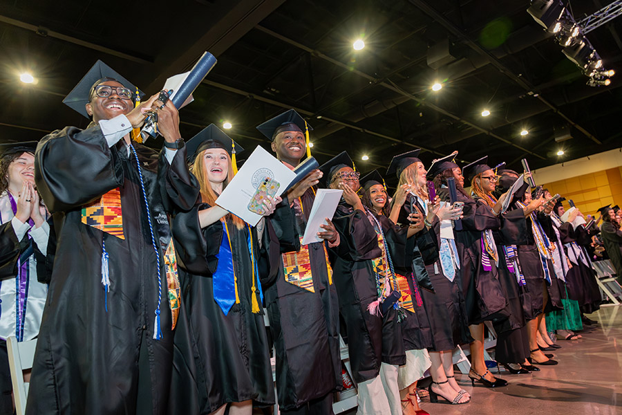 Male and female students standing in graduation caps and gowns smiling. 