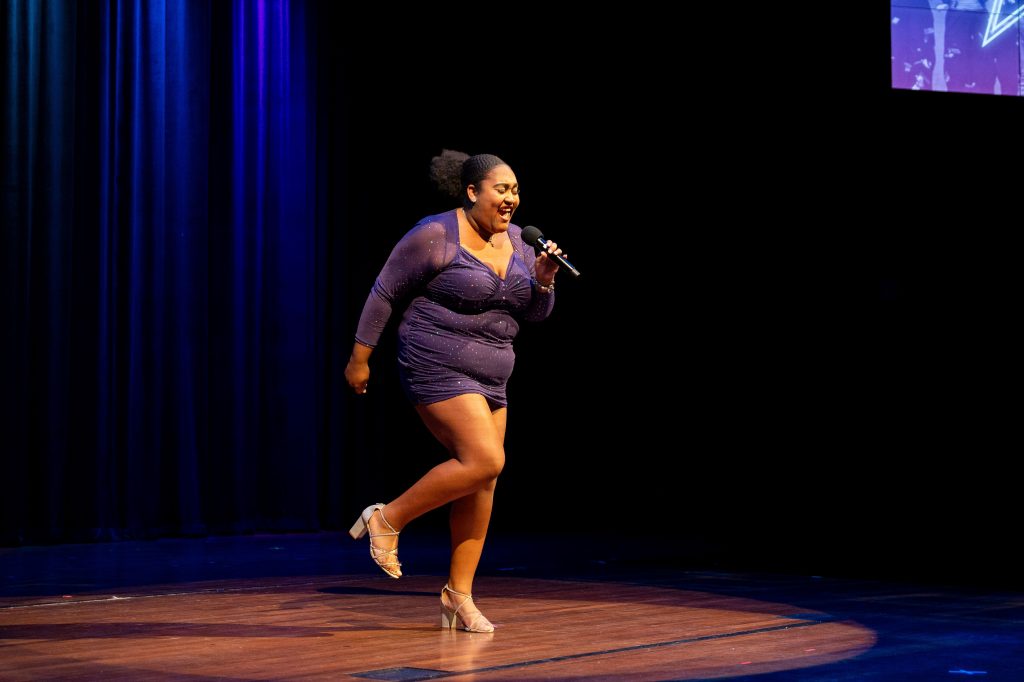 A woman on stage holds a microphone while singing.