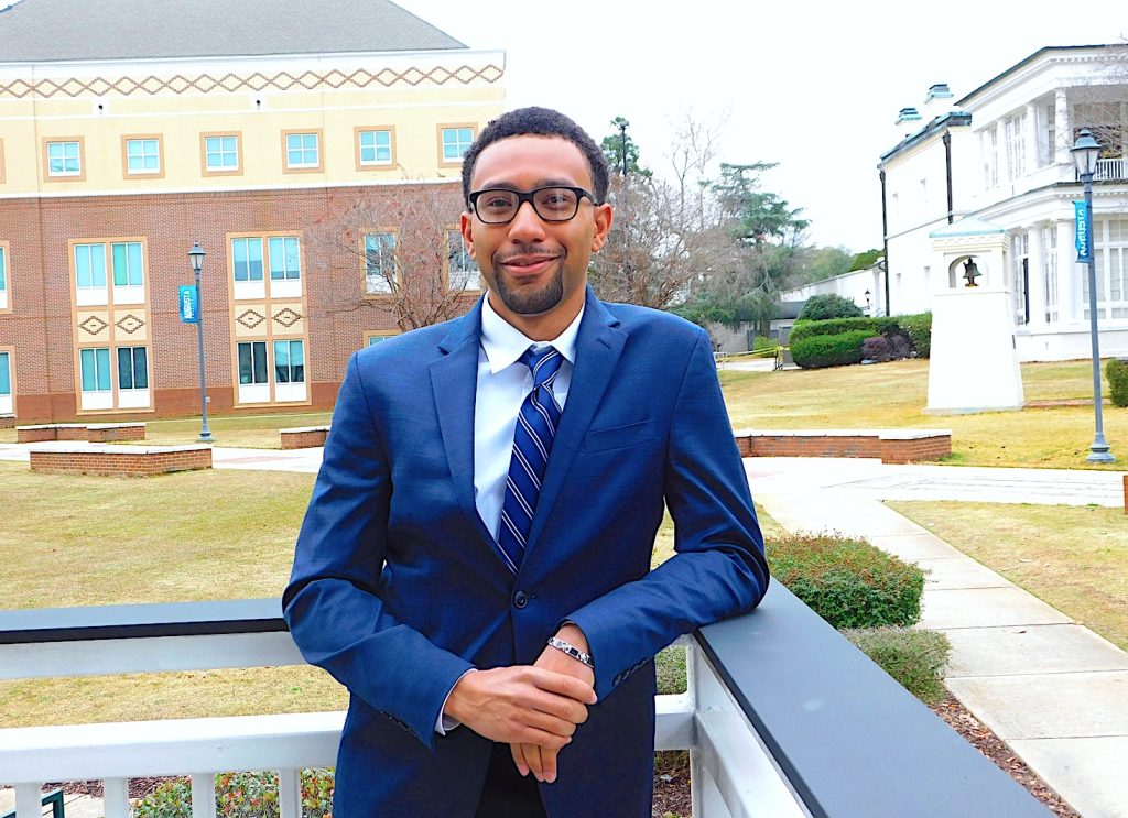 A male college student wearing a suit standing outside on a college campus.