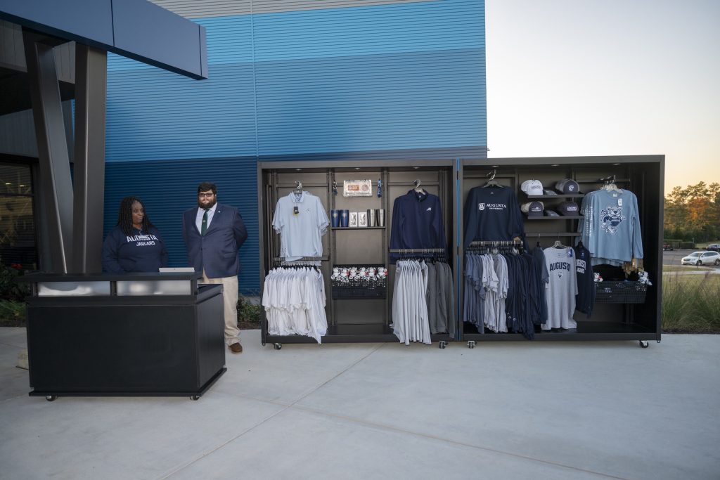 Two college students, ones man and one woman, manage a merchandise booth during an outdoor event.