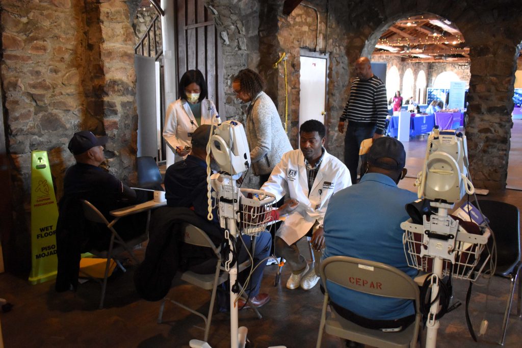 A group of people in lab coats perform blood pressure screenings