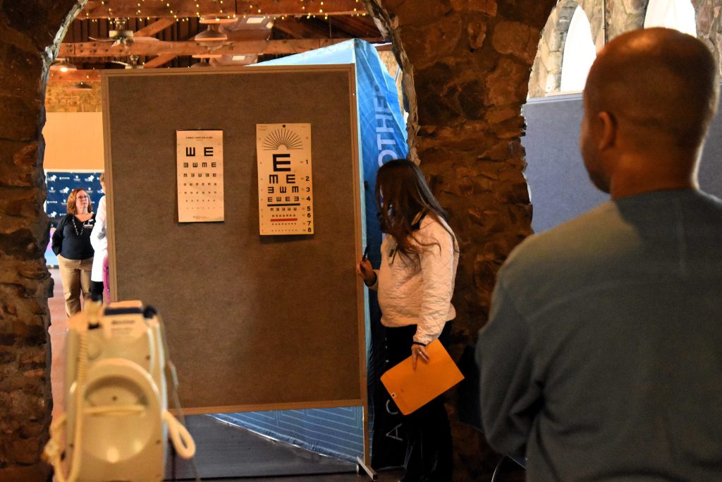 A man takes a vision test, with the vision cards pinned to a poster board display