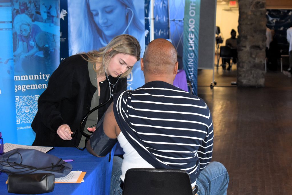 A woman performs a blood pressure check on an older man, neither are facing the camera