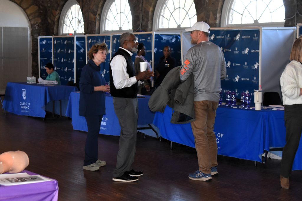 A man and a woman speak to a man in a baseball cap in front of blue vendor tables
