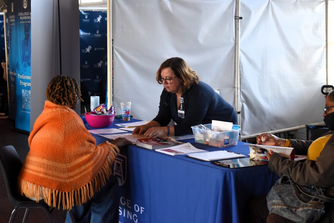 A woman leans over a table, explaining information to a grandparent