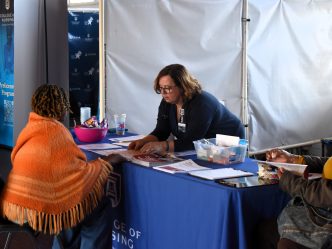 A woman leans over a table, explaining information to a grandparent