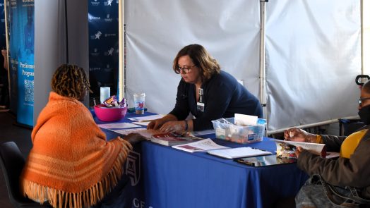 A woman leans over a table, explaining information to a grandparent