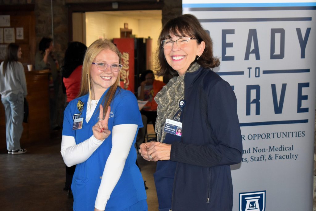 A young woman holds up a peace sign, posing beside a another smiling woman