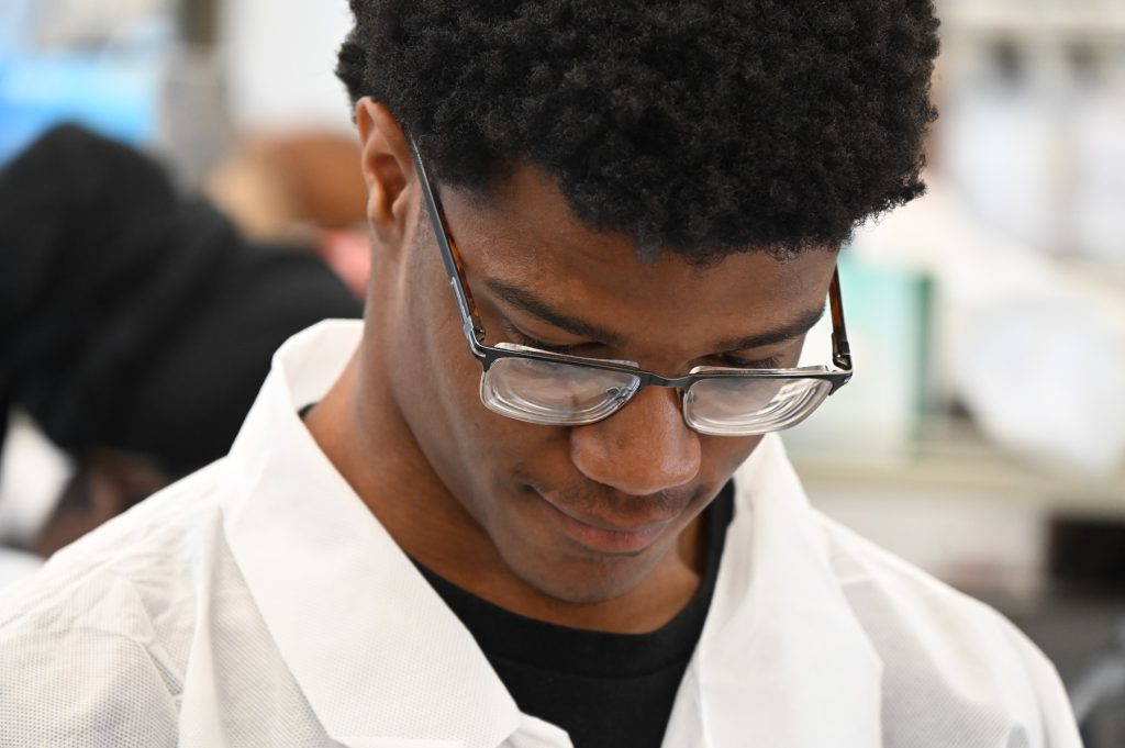 This is a photo of a high school student using lab equipment to learn about cancer research.