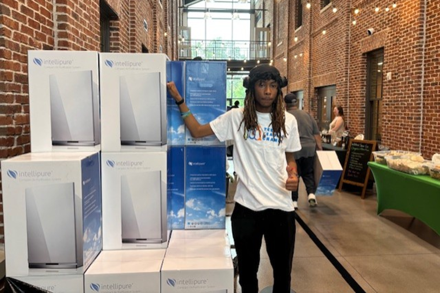 A male high school student stands next to a stack of boxes for brand new air purifiers.