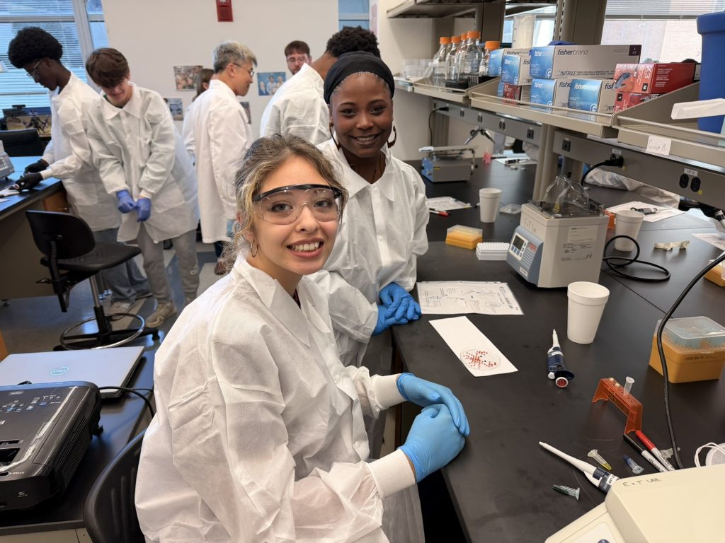 In this photo, you see students posing for a picture while working with research lab equipment.
