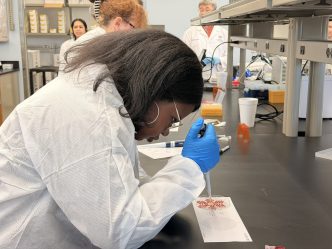 A female high school student learns how to use lab equipment during a field trip to a scientific lab.