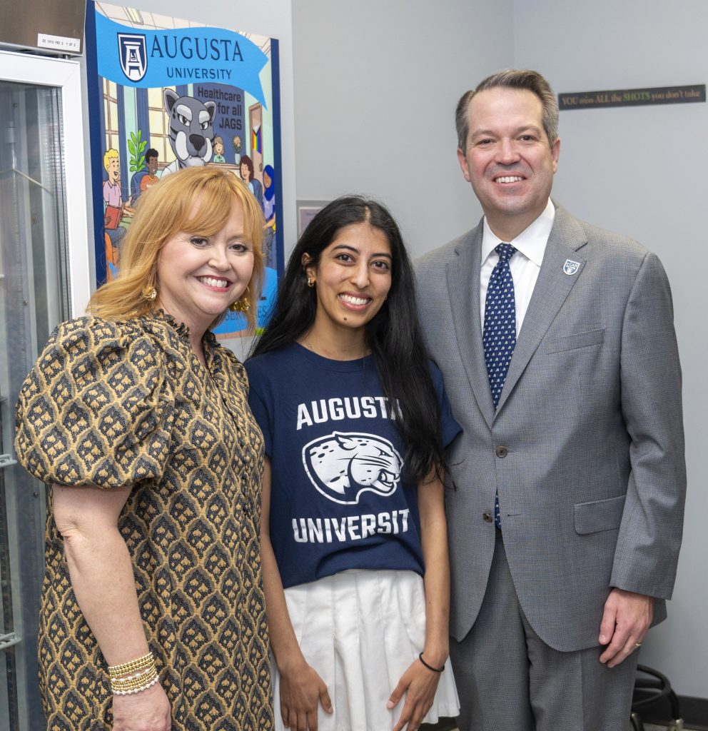 Two women and a man pose for a photo in front of a wall mural.