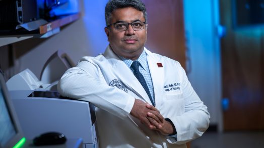 A male scientist stands in a lab surrounded by computers and other lab equipment.