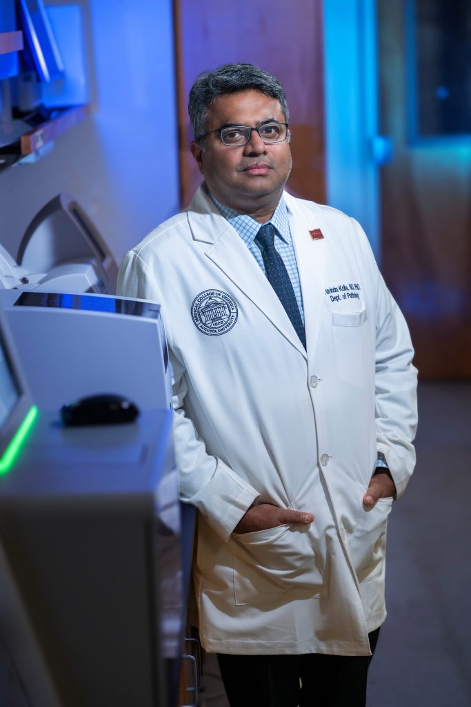 A male scientist stands in a lab surrounded by computers and other lab equipment.