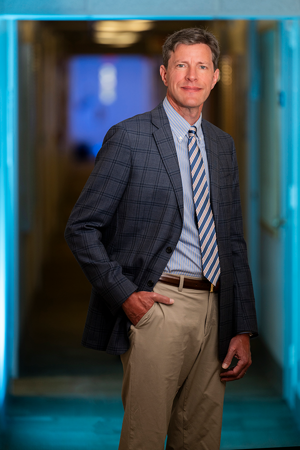 A man stands in the hallway of a building on a college campus.