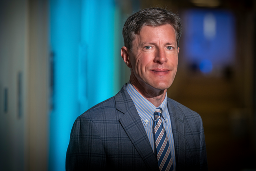 A man stands in the hallway of a building on a college campus.