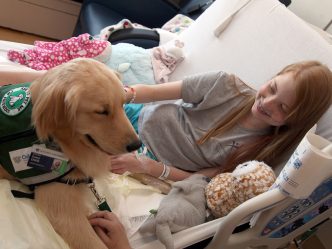 Girl in hospital bed with therapy dog.