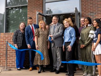 A group of people stand behind a ribbon with the center man holding scissors.