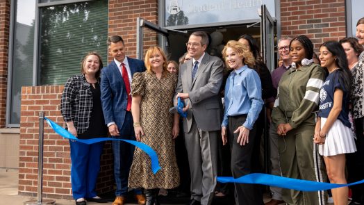 A group of people stand behind a ribbon with the center man holding scissors.