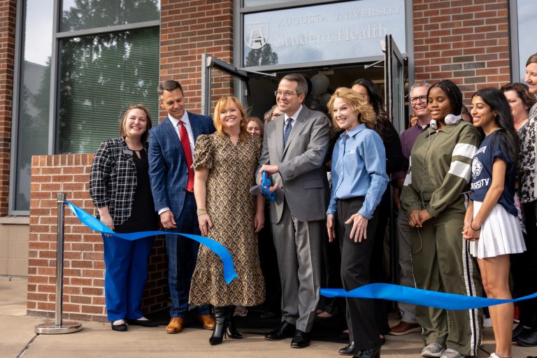 A group of people stand behind a ribbon with the center man holding scissors.