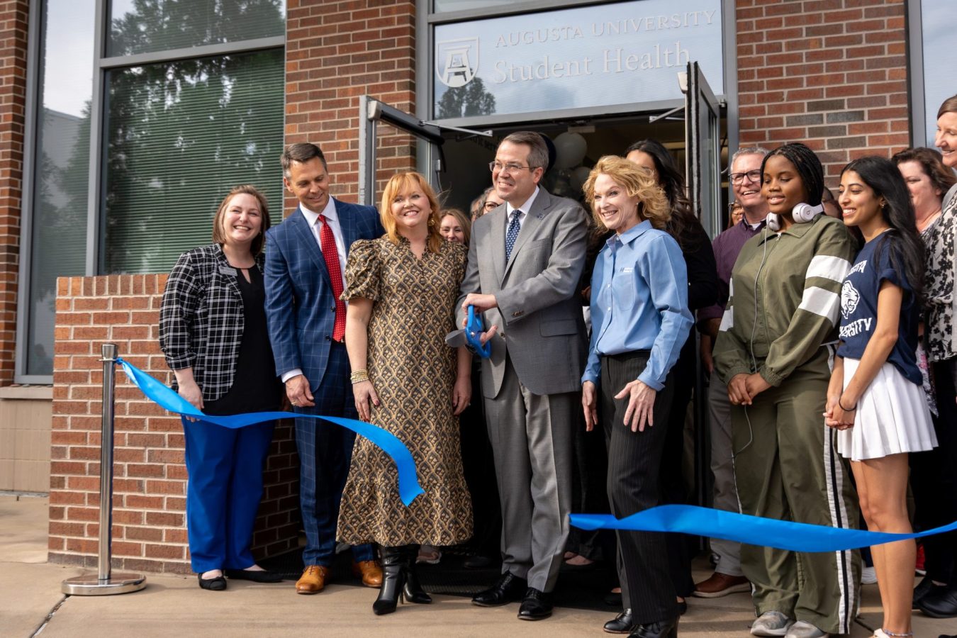 A group of people stand behind a ribbon with the center man holding scissors.