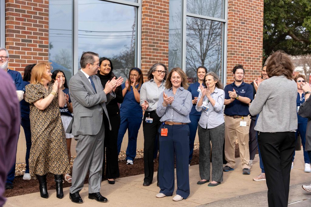 A group of men and women smiling and clapping while outdoors.