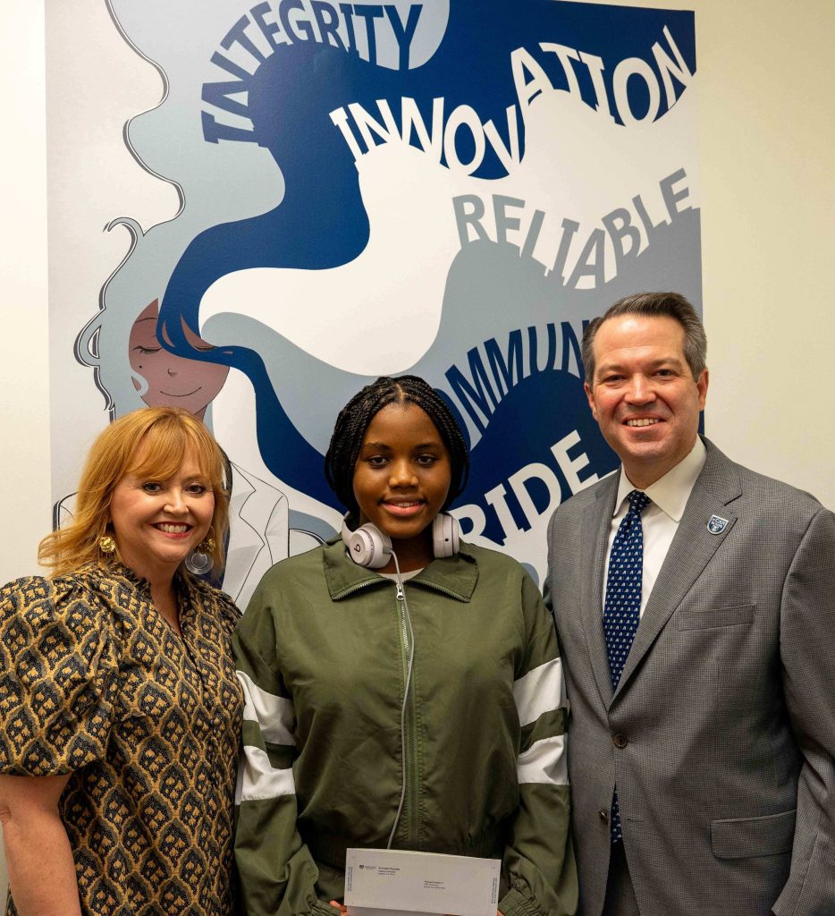 Two women and a man pose for a photo in front of a wall mural.