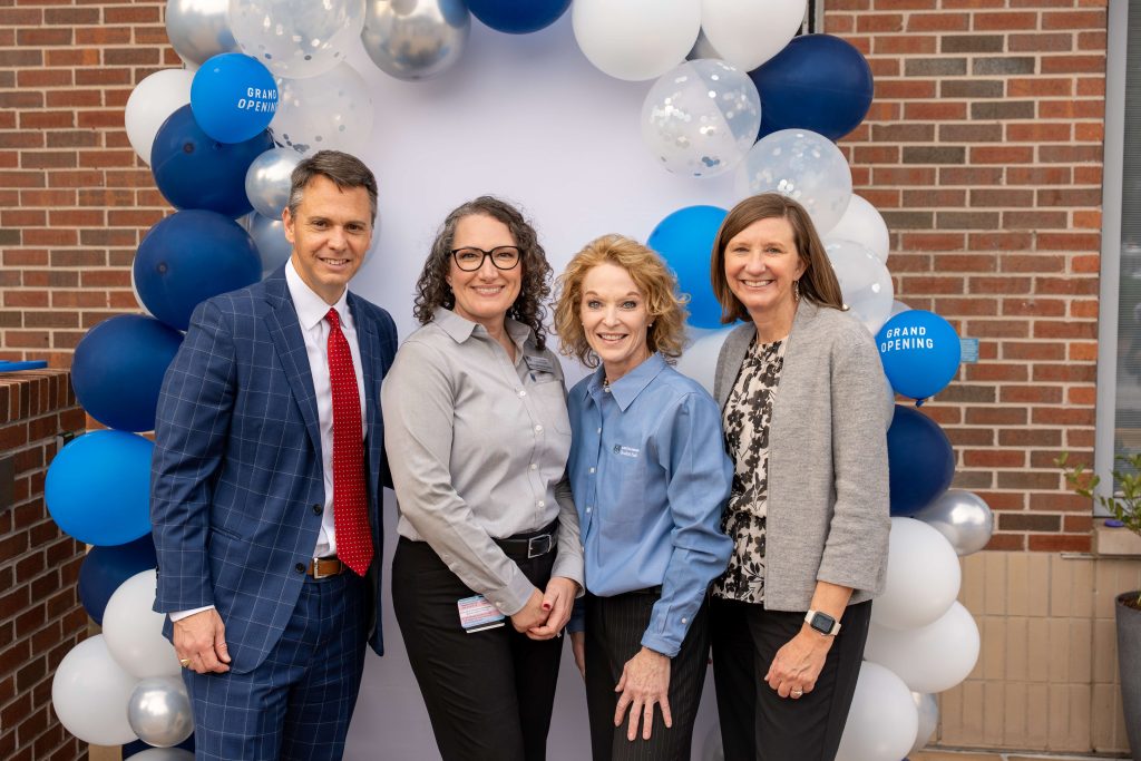 A man and three women pose for a photo in front of a balloon arch.