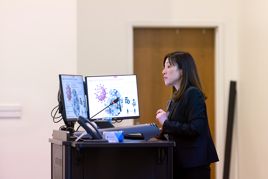 A woman presents to a large crowd in a modern lecture hall on a college campus.