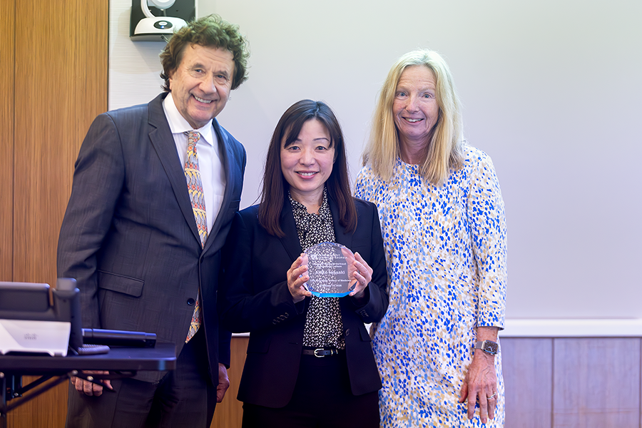 A man and a woman present another woman with an award.