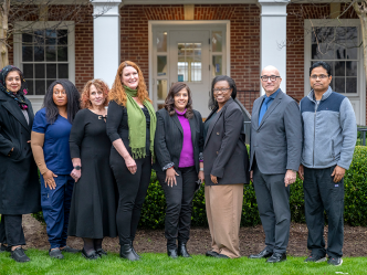 A group of doctors stands in front of an older building on a hospital campus.