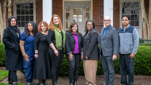 A group of doctors stands in front of an older building on a hospital campus.