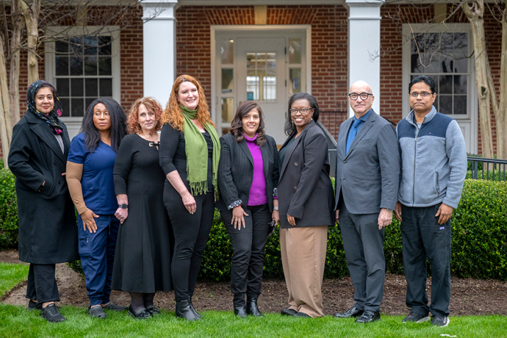 A group of doctors stands in front of an older building on a hospital campus.