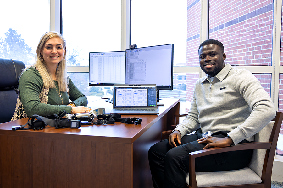 A female college professor and a male student look over data on a laptop computer. there are several pedometers on the desk in front of them.