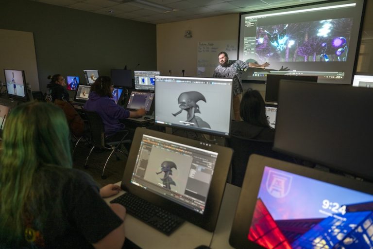 students on monitors looking at a male teacher present work on a board