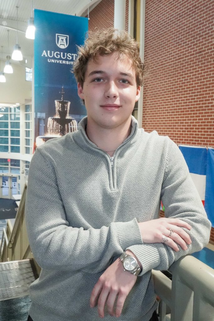 With an arm propped on a stairwell, a guy smiles for a photo.