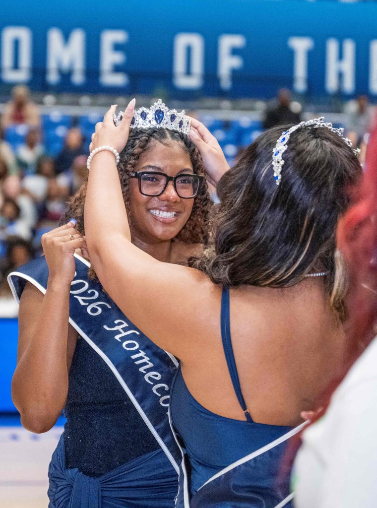 A woman places a crown on the top of another woman's head.