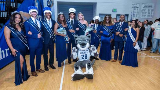 Men and women dressed in formal form a semi-circle around Augusta University's mascot Augustus.