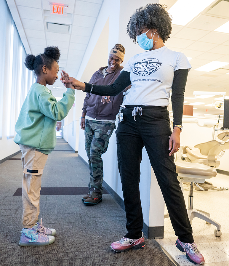 A dental hygienist gives a high five to a young girl. A former NFL football player smiles in the background.