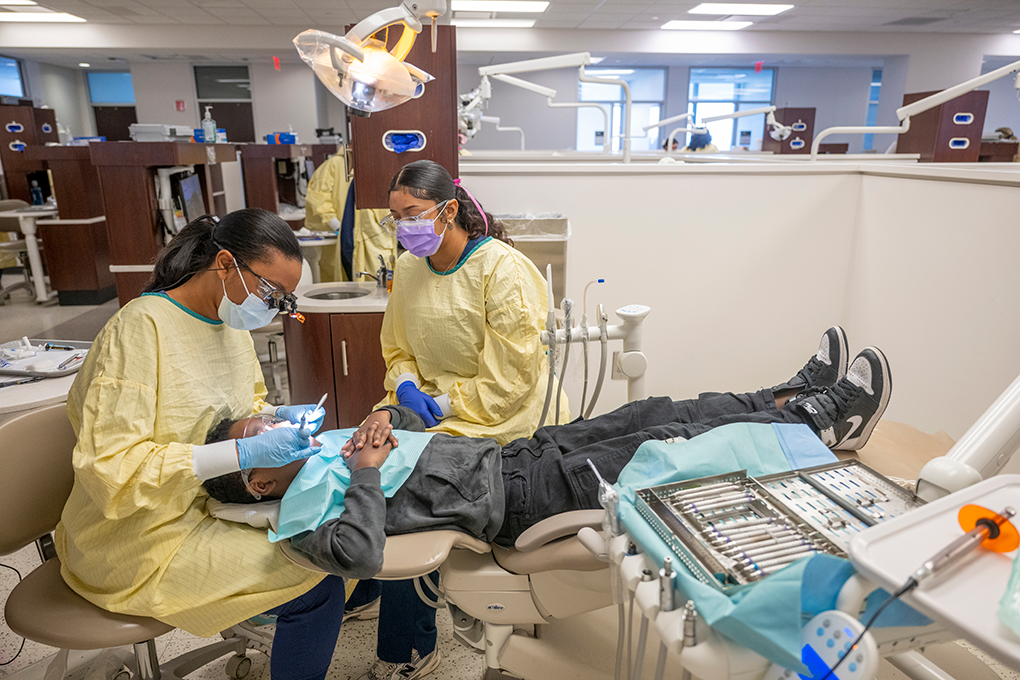 Two female dental hygiene students clean a young boy's teeth.