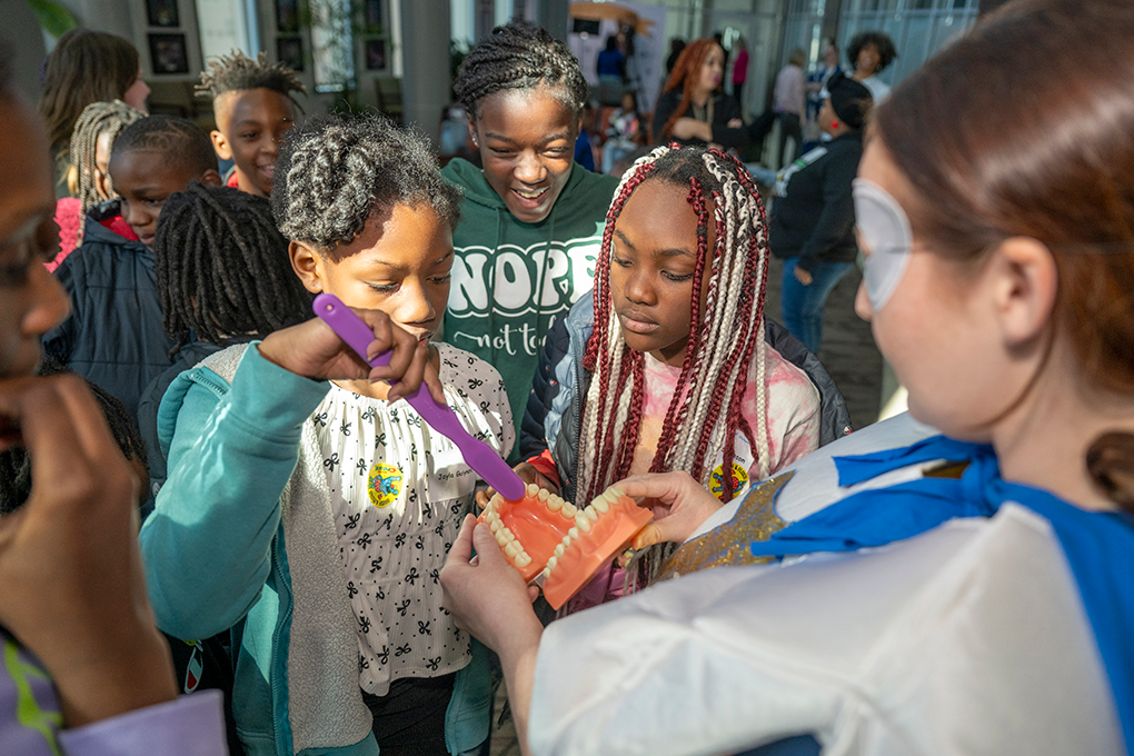 A group of elementary school children practice brushing teeth using a mouth model.
